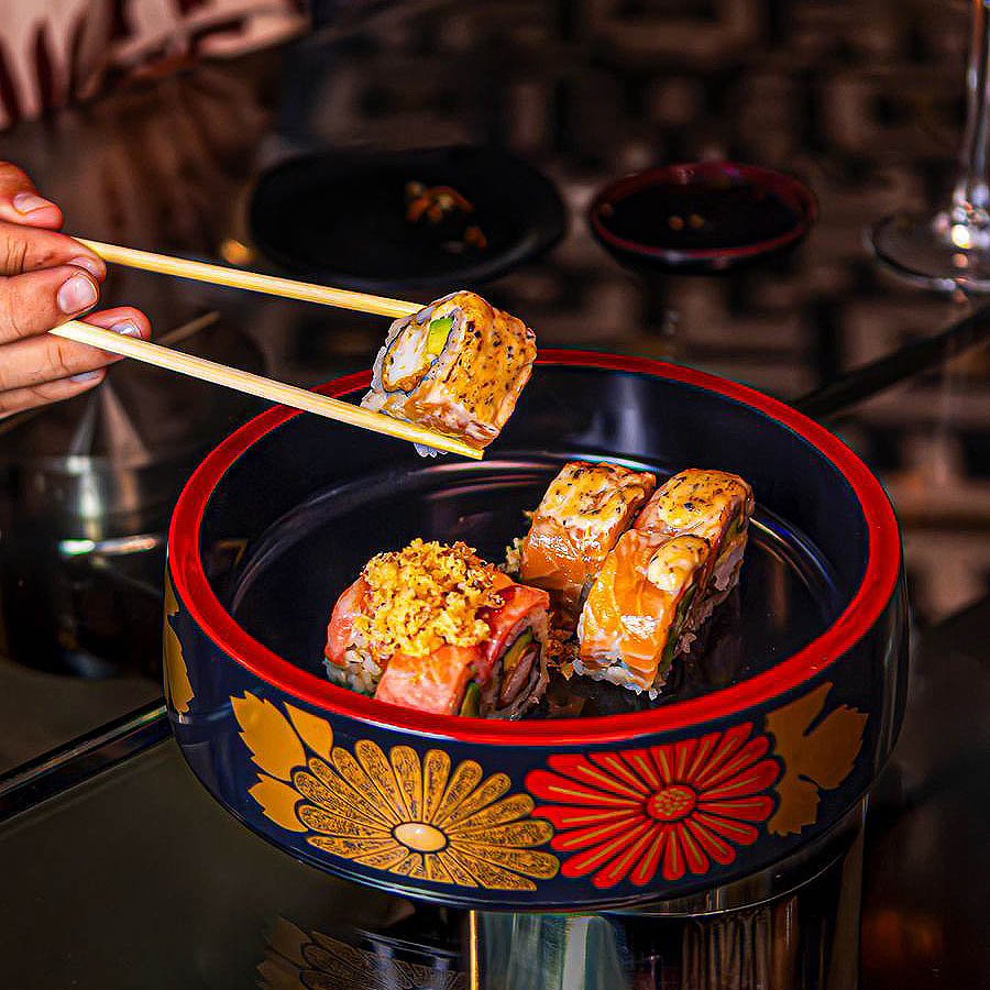 Pieza de roll de sushi tomada con palillos sobre bowl decorado